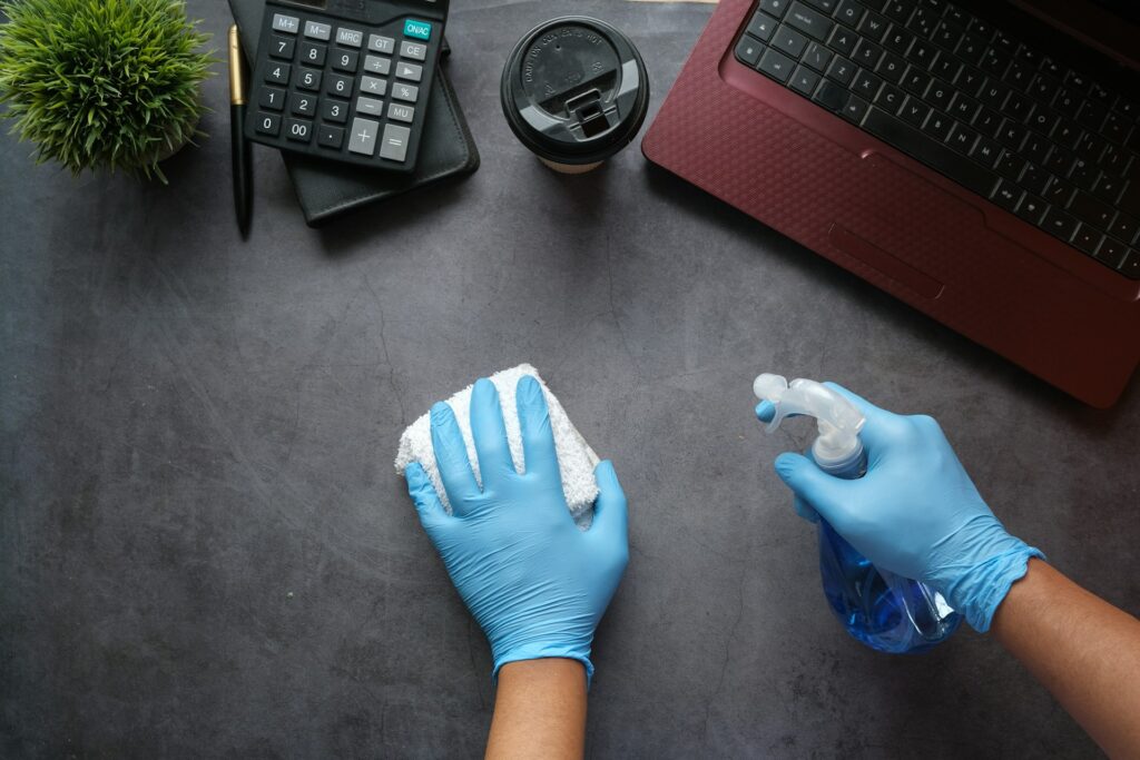 Gloved hands wiping a desk with spray cleaner, reflecting the quote: ‘A clean office creates a clear mind.