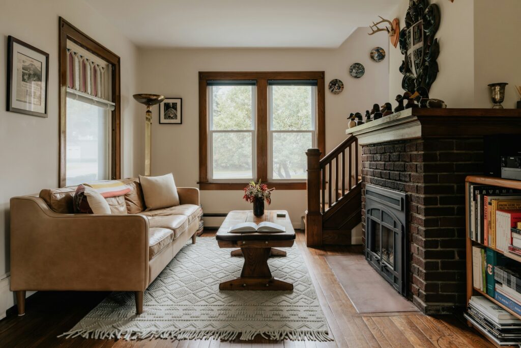 Cozy living room with a brick fireplace, wooden floors, and natural light, illustrating a common home setting where homeowners ask how to clean your brick fireplace to keep it looking fresh and well maintained. Image by Clay Banks via www.unsplash.com