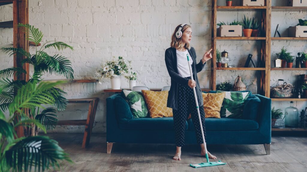 Woman cleaning her living room floor with a mop in a cozy, plant-filled apartment, representing eco-friendly home care using a white vinegar carpet cleaner. Image by Vitaly Gariev via www.unsplash.com